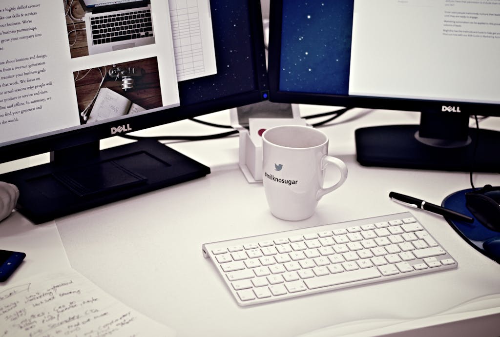 A contemporary workspace featuring dual Dell monitors, a keyboard, and a Twitter mug.
