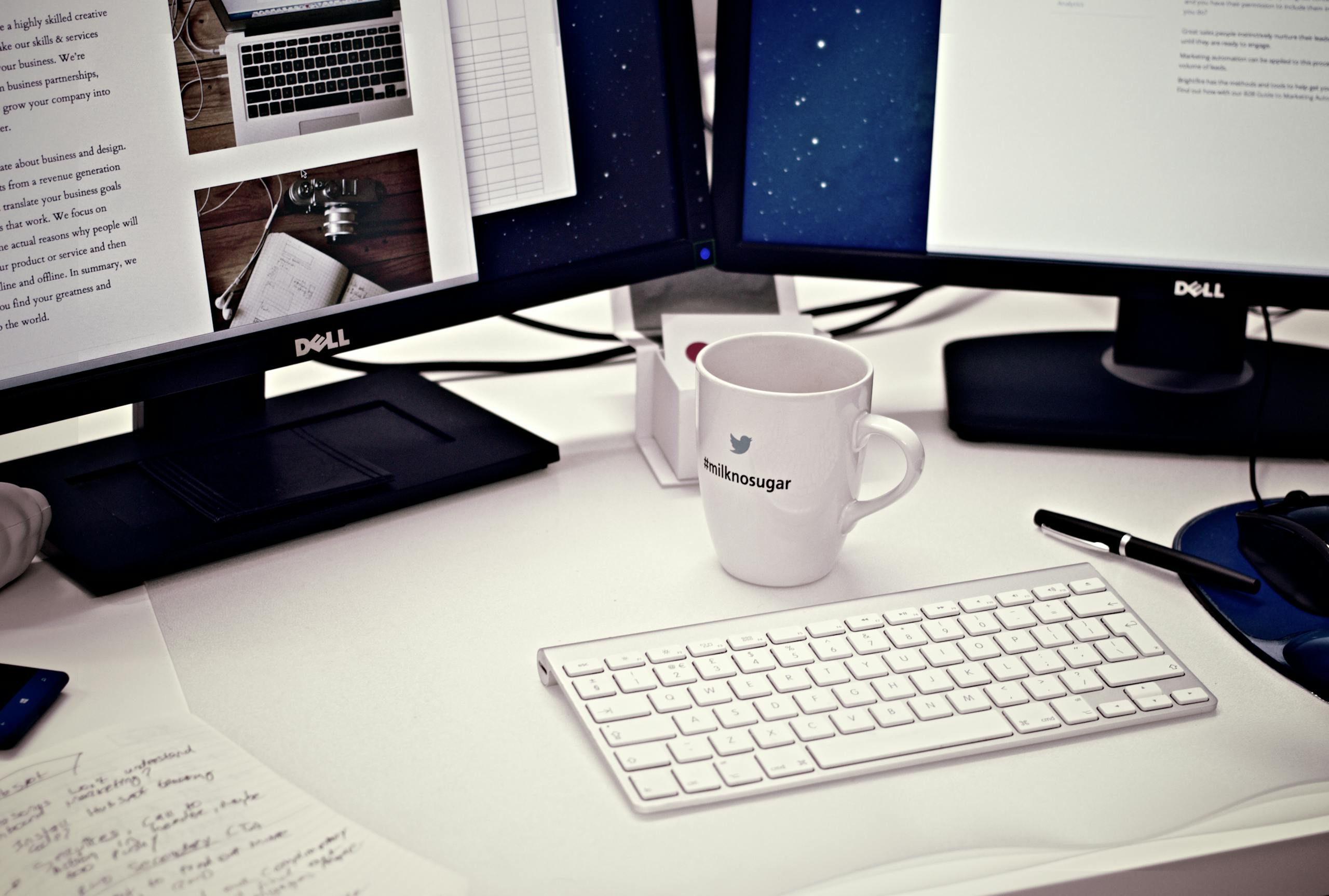 A contemporary workspace featuring dual Dell monitors, a keyboard, and a Twitter mug.