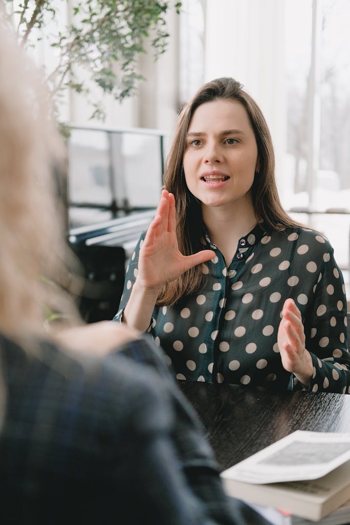 Focused woman in a polka dot blouse engages in a conversation indoors.